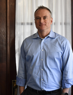 Chris Foley, medium shot, wearing a blue buttonup shirt, with hands in his pockets.